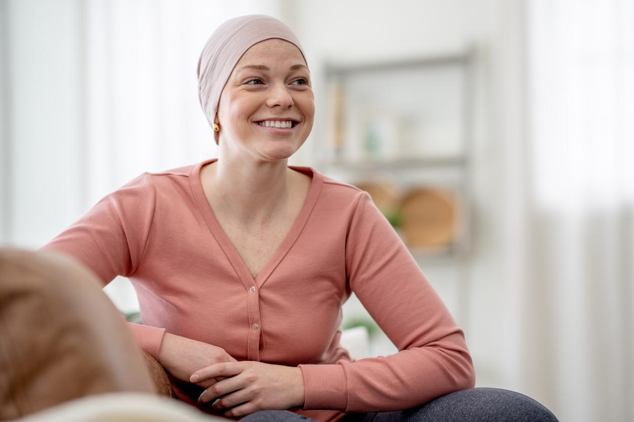 A young woman battling cancer sits in the comfort of her own home between treatments as she poses for a portrait. She is dressed comfortably and wearing a headscarf to keep warm.