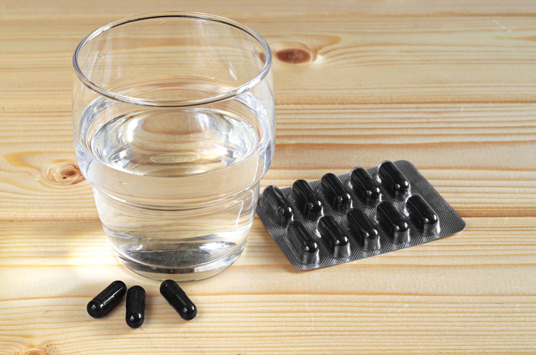 Medical capsules with activated charcoal and glass of water on wooden table