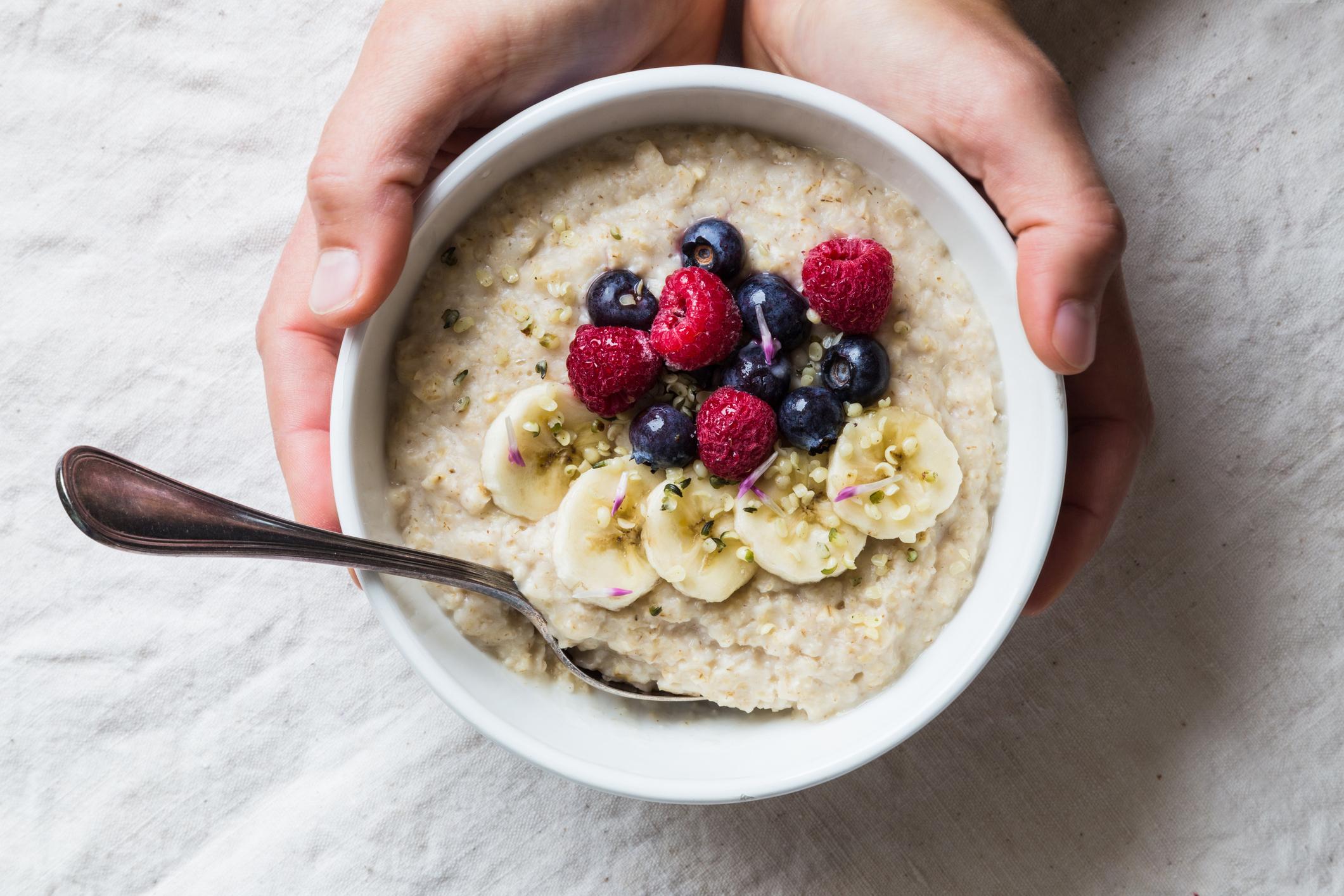 Pair of hands holding a bowl of oatmeal with fruit and berry topping.